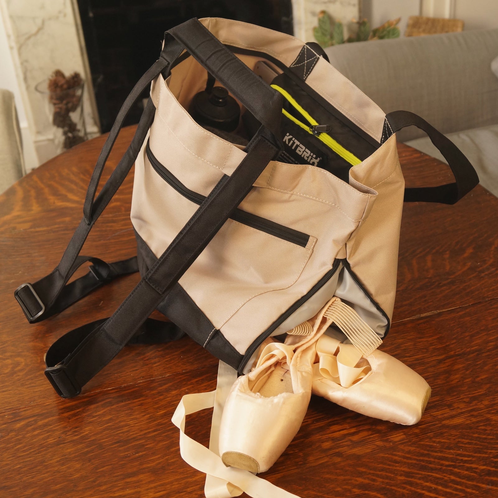 Beige bag with straps on a wooden table, with ballet shoes inside.