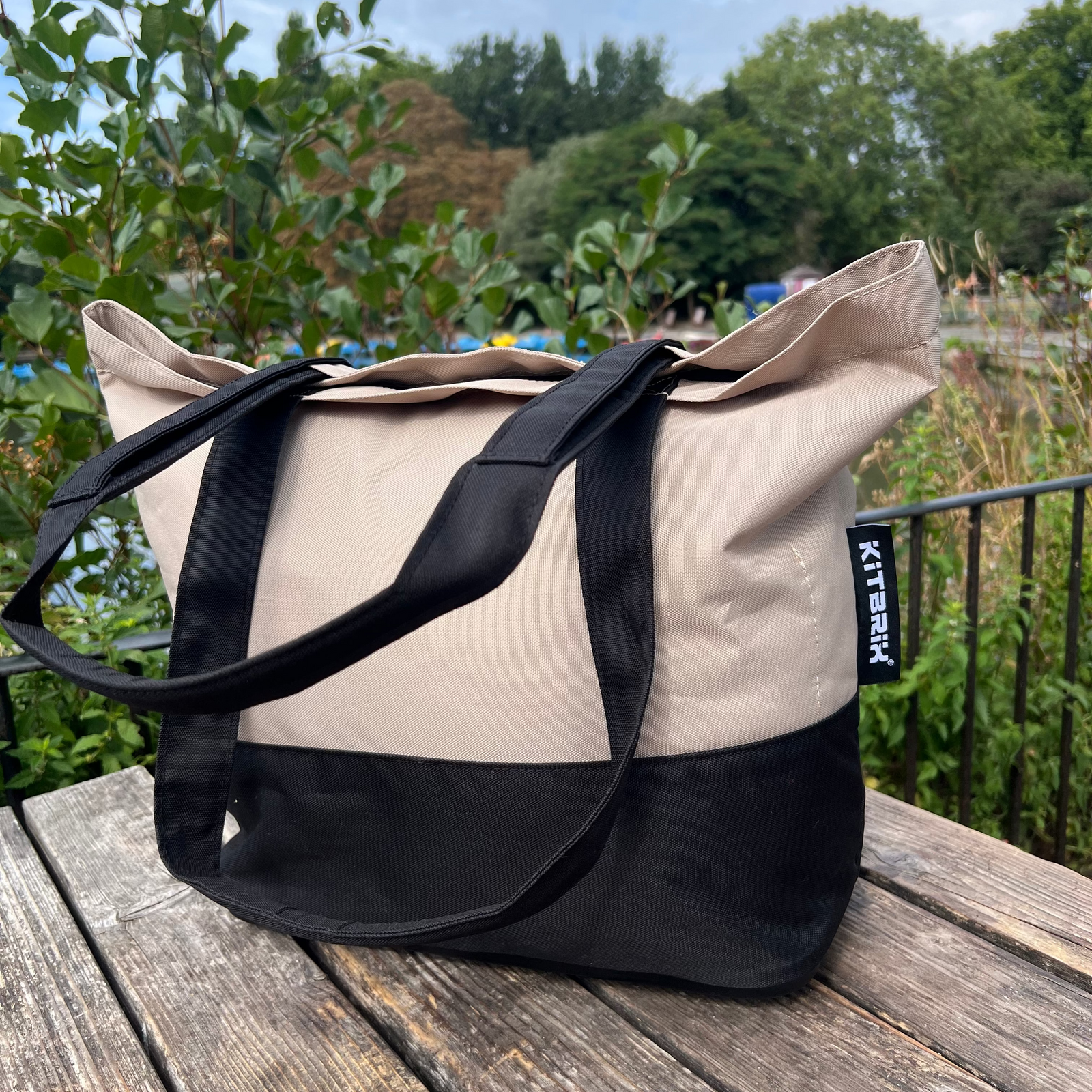 Beige and black tote bag on a wooden surface with a garden background