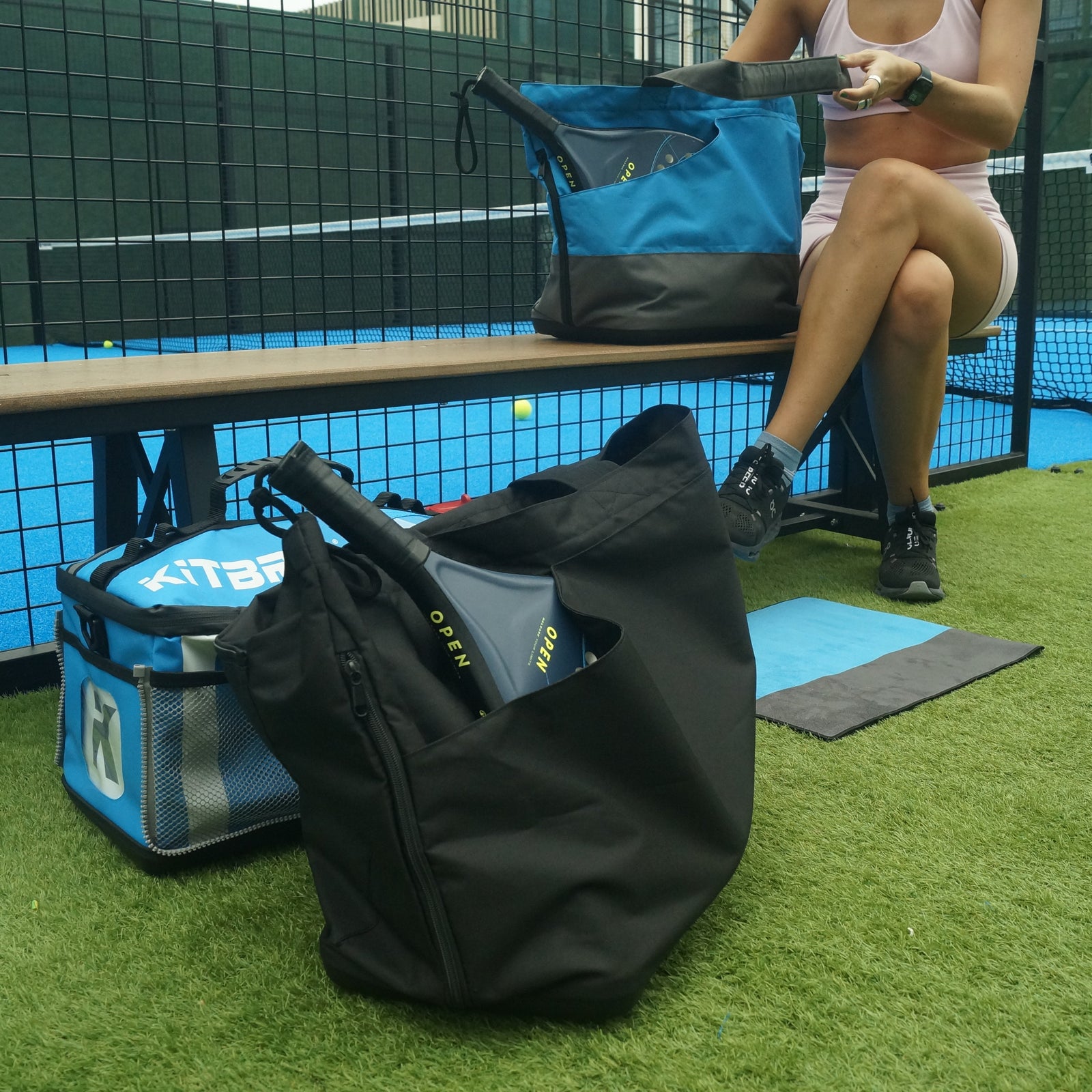 Person sitting on a bench with sports bags on a tennis court