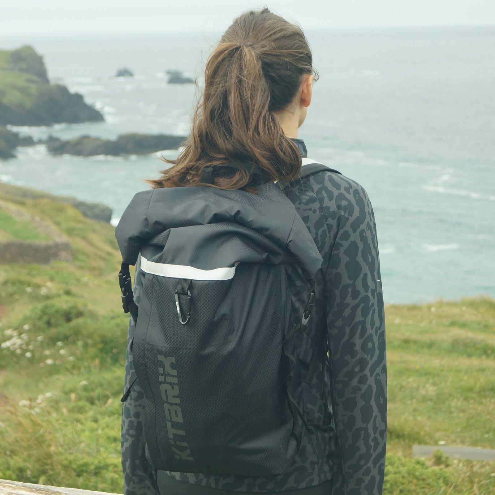 A girl wearing a black jacket with KitBrix Pokit daypack by the sea