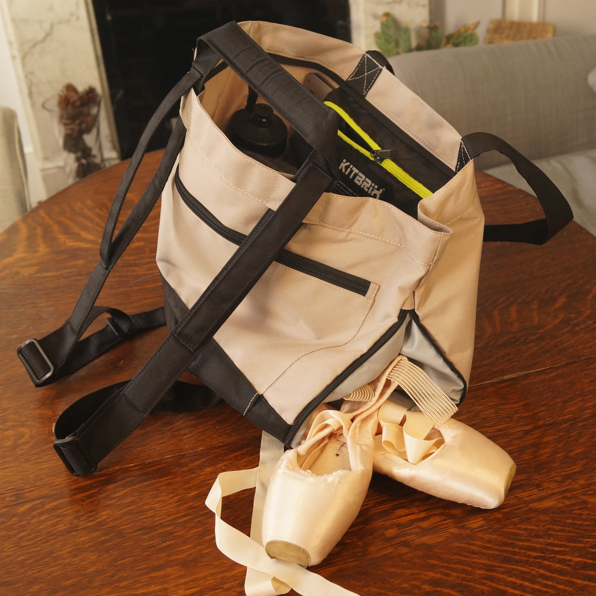 Beige bag with straps on a wooden table, with ballet shoes inside.