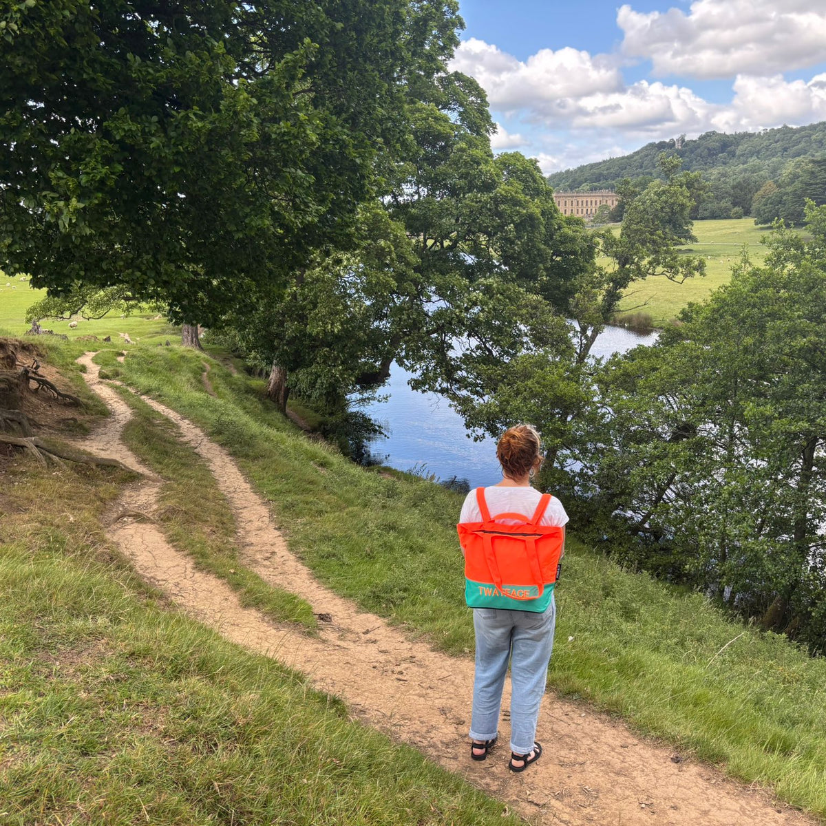 A women with a tote bag standing on a path overlooking a scenic landscape with trees and a lake.